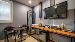 Ein Hotelzimmer mit Schreibtisch, Stühlen, einem Flachbildfernseher, einer Minibar und einem Bett.