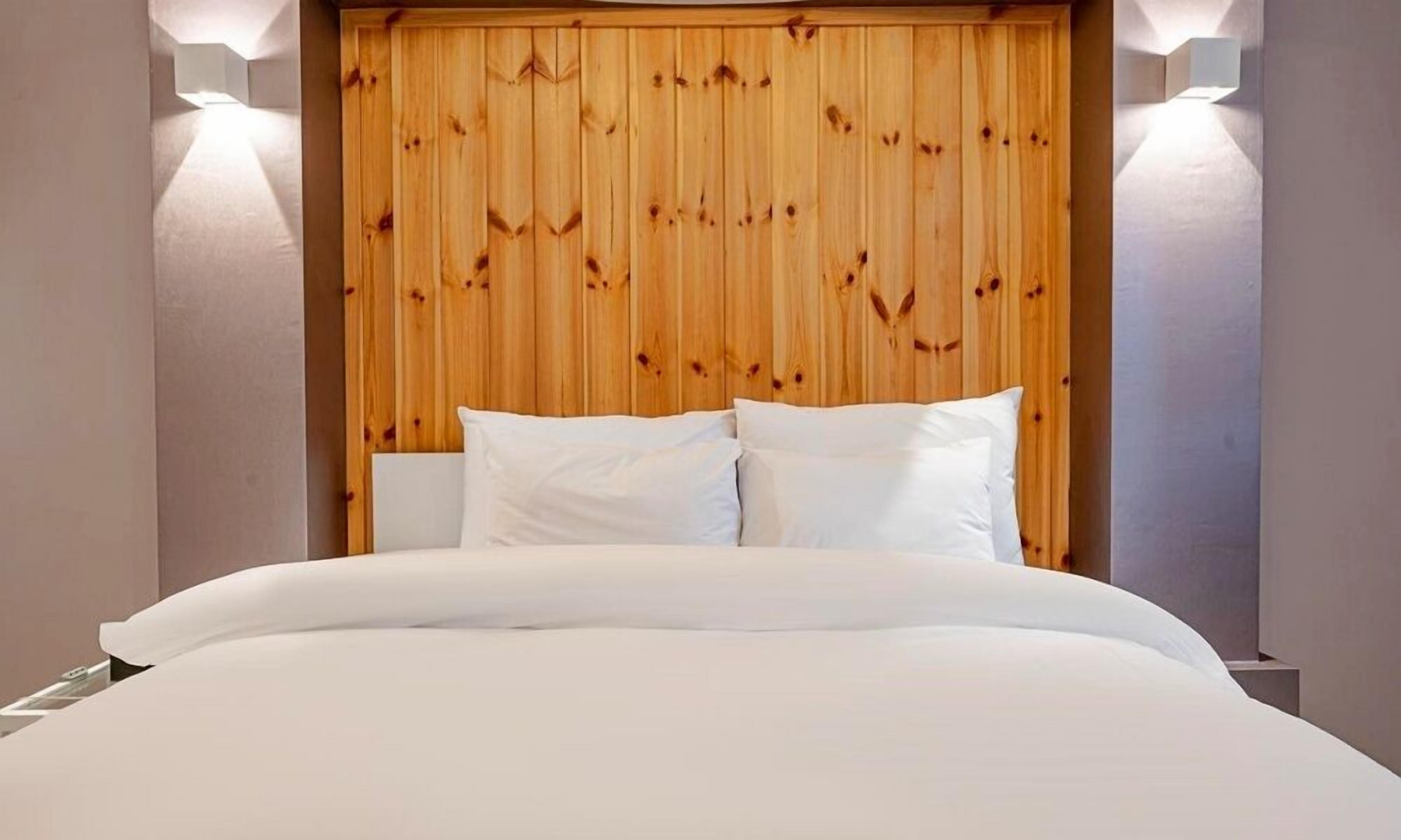 A hotel room with a wooden headboard, white bedding, and two wall-mounted lights.