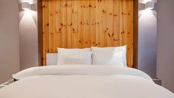Habitació d'hotel amb capçal de llit de fusta, roba de llit blanca i dues làmpades de paret.
