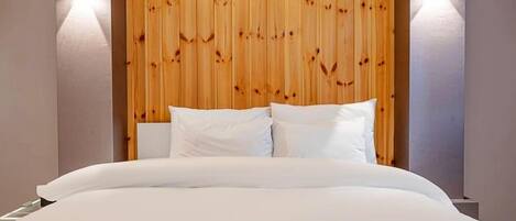 A hotel room with a wooden headboard, white bedding, and two wall-mounted lights.