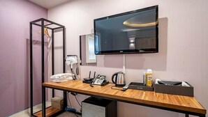 Ein Hotelzimmer mit Holzschreibtisch, Flachbildfernseher, Telefon, Wasserkocher und Minibar.
