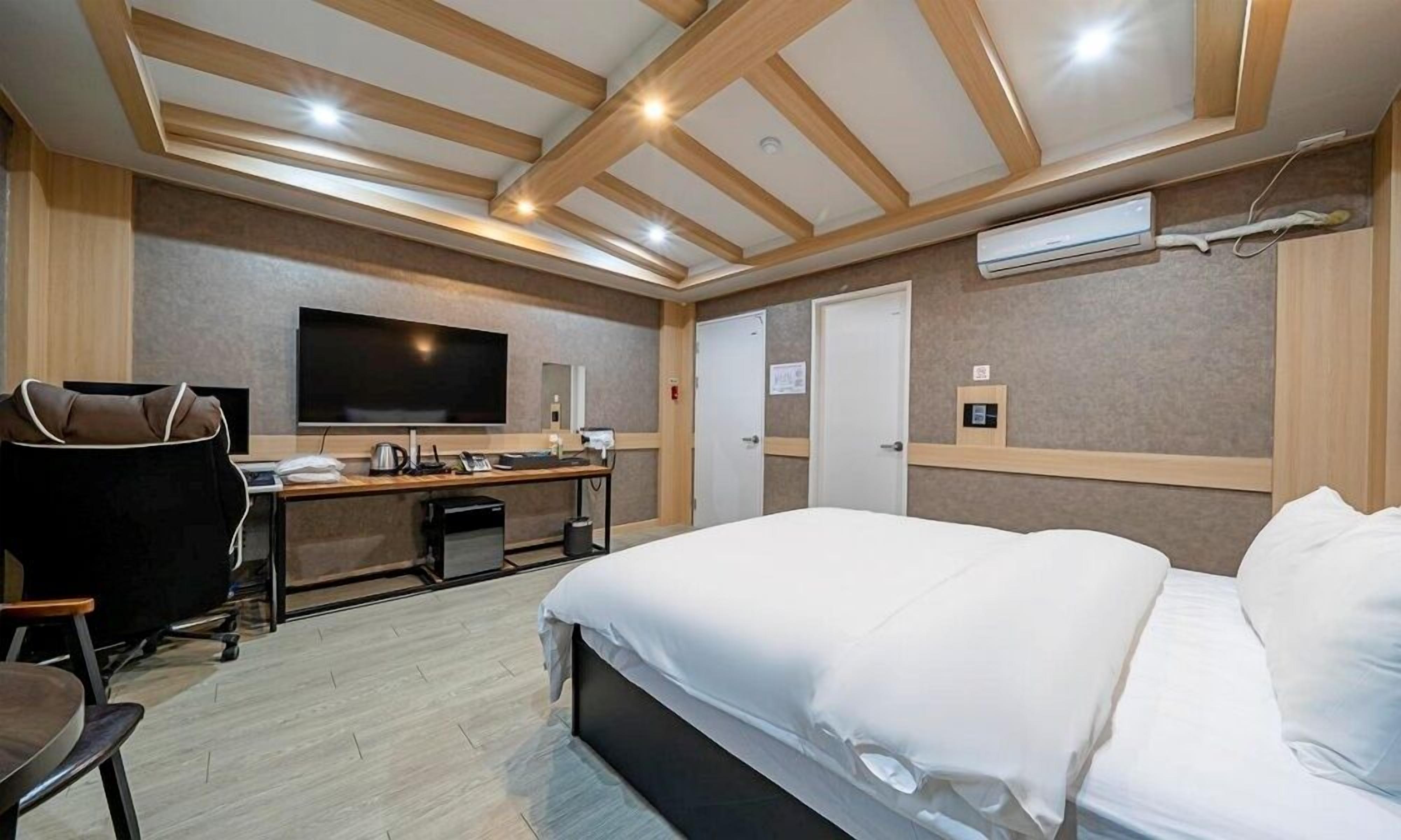 A hotel room with a bed, a desk with a TV, a chair, and a wardrobe.