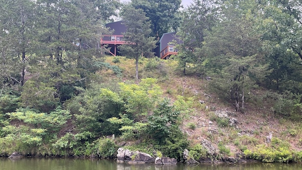 A house with a red balcony overlooking a lake, surrounded by dense trees. - The Aspen at Hamilton Cove ~ Cabin Eleven ~ Pet Friendly (Royal)