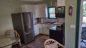 A compact kitchen with a refrigerator, sink, and cabinets. There are wicker chairs and a small dining table. - The Aspen at Hamilton Cove ~ Cabin Eleven ~ Pet Friendly (Royal)