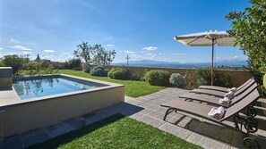 Piscina com vista para montanhas, rodeada por um terraço com espreguiçadeiras e um guarda-sol.