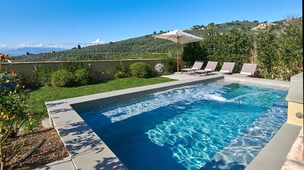 Piscina com água azul cristalina, rodeada por um terraço com espreguiçadeiras e um guarda-sol.