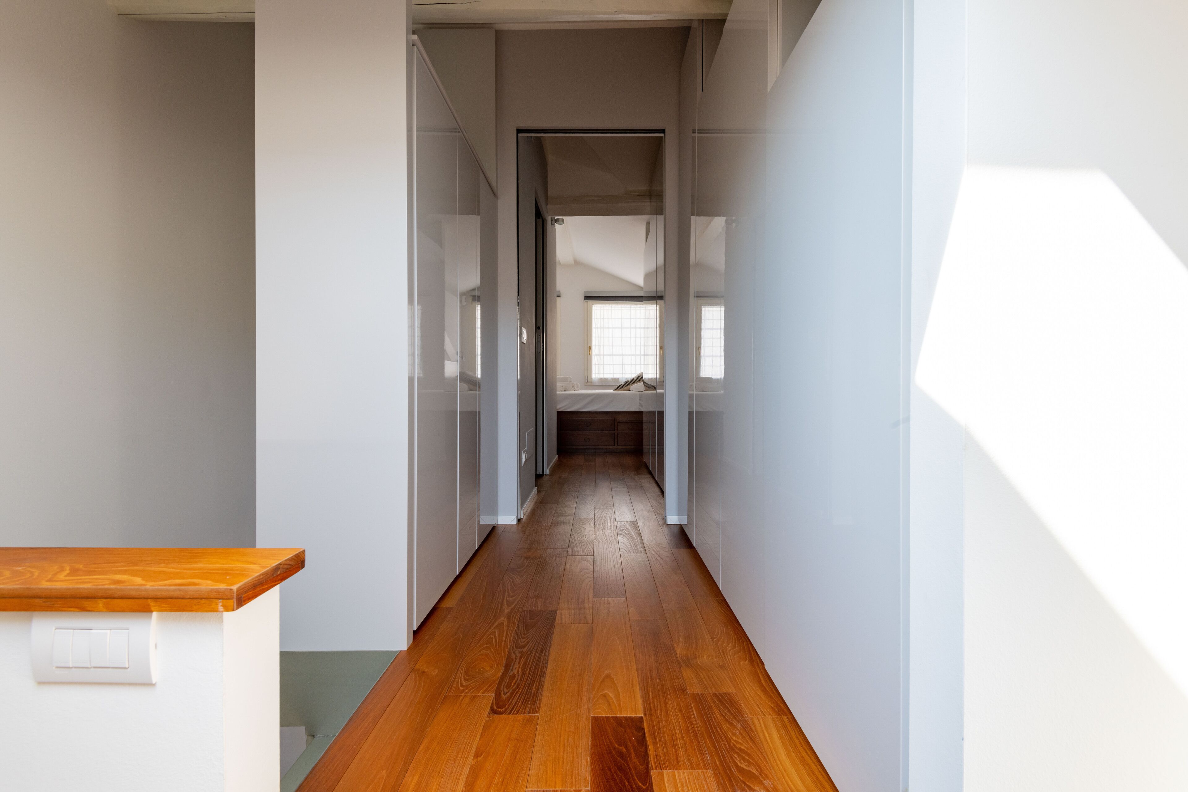 Un pasillo estrecho con suelo de madera y paredes blancas.