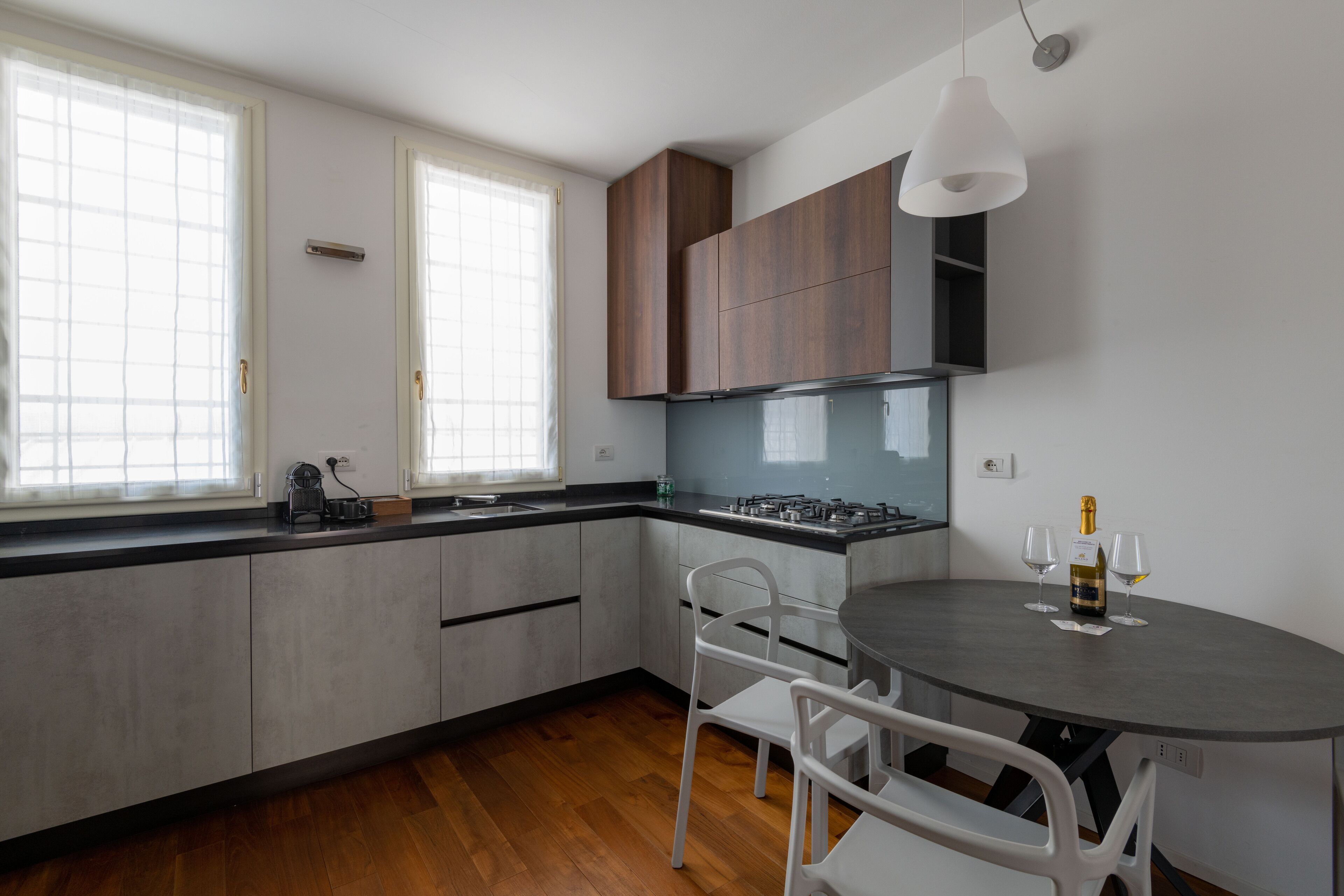 Una cocina moderna con comedor, que incluye una mesa redonda, dos sillas, una botella de vino y copas.