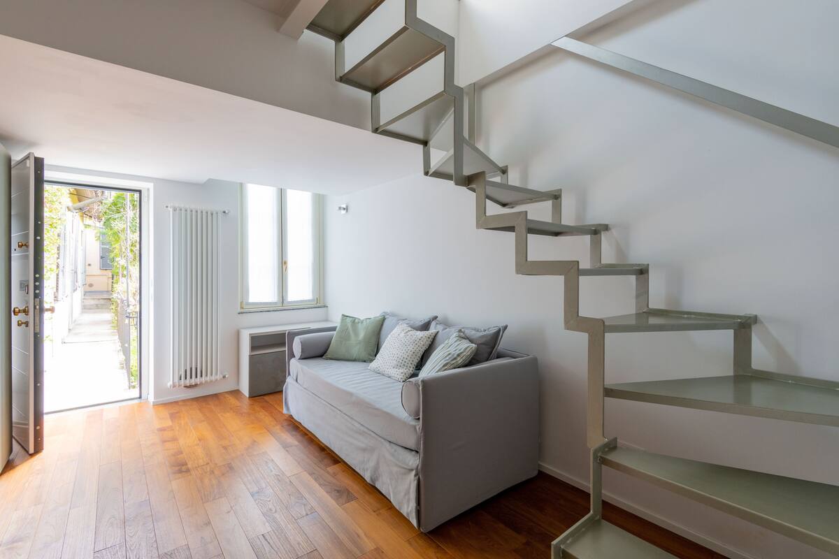 A modern living room with a grey sofa, a glass staircase, and a wooden floor.