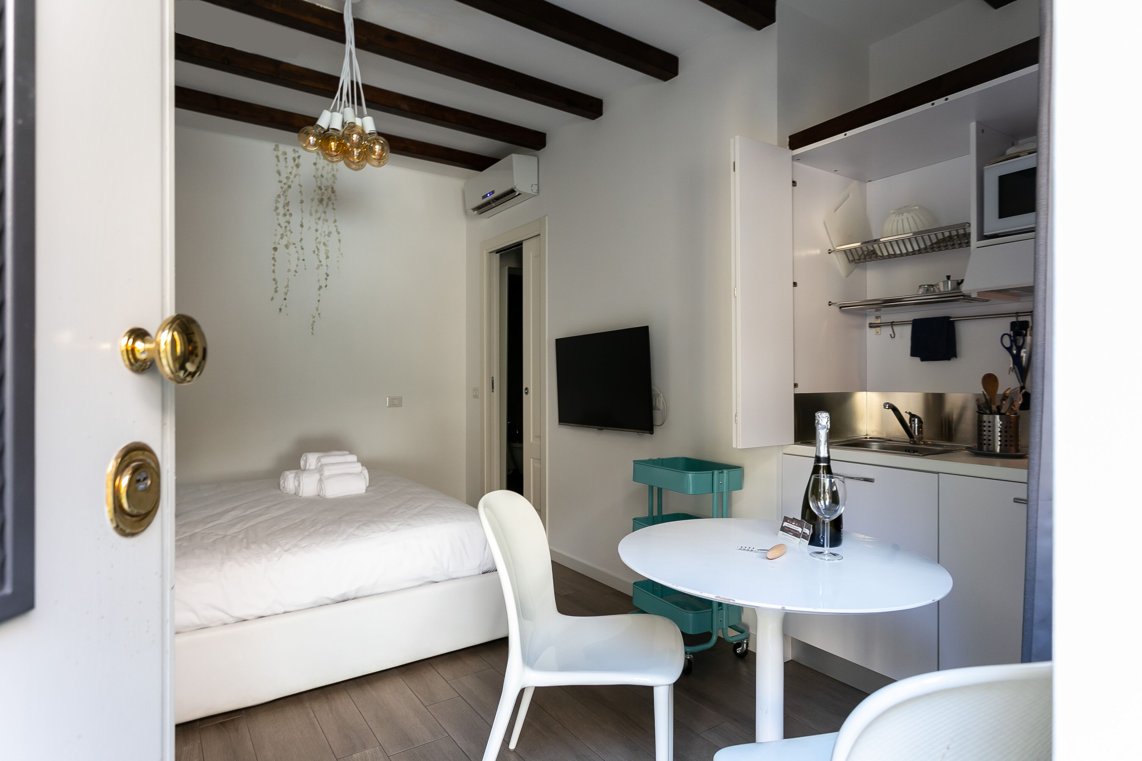 Una habitación funcional con cama, una pequeña mesa de comedor, televisor y kitchenette.