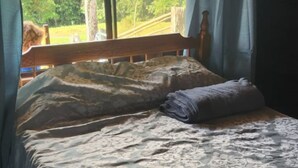 Een slaapkamer met een bed, gordijnen en uitzicht op groen.