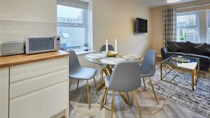 A modern kitchen with a microwave, dining table, and chairs. There is a sofa and a TV in the living area. - Host & Stay | Studio No.8 (Alnwick)