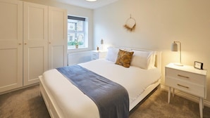 A bedroom with a large bed, a window, a wardrobe, and a bedside table with a lamp. - Host & Stay | Studio No.8 (Alnwick)