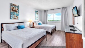 Doble habitación con dos camas, un escritorio, una lámpara y obras de arte en las paredes.