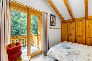 Ein Schlafzimmer mit einem Bett, einem Holzkopfende, einem Fenster mit Vorhängen und Blick auf einen Balkon.