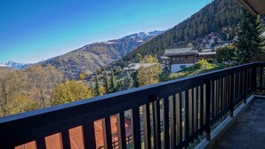 A balcony with a view of a mountainous landscape, a red building, and a wooden fence. - Arnica 1 - 6 pers - piscine (Haute-Nendaz)