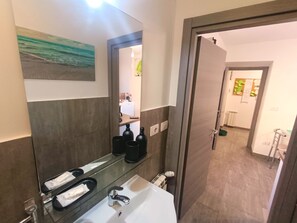 A bathroom with a white sink, a mirror, and a towel rack. There are black bottles on the counter.