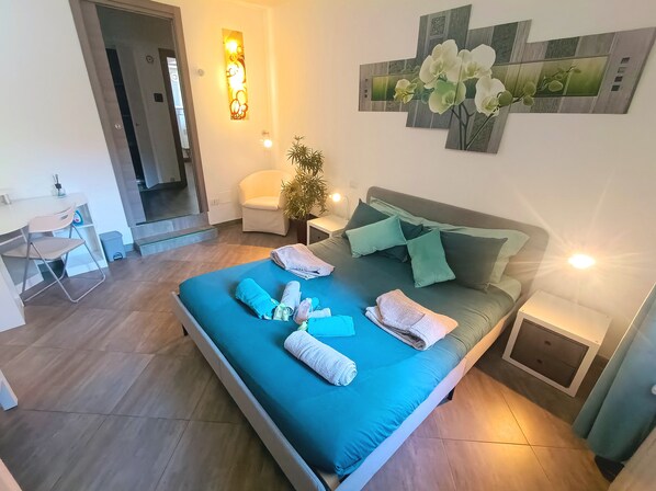 A bedroom with a bed, pillows, a nightstand, a chair, a desk, and a wall-mounted artwork.