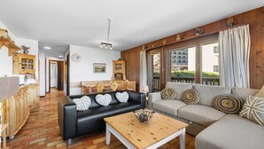 A cozy living room with a black leather sofa, a grey sofa, and a wooden coffee table. There are wooden cabinets and a clock on the wall.