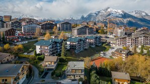 A mountain resort with multiple multi-story buildings, a ski lift, and snow-capped mountains in the background.