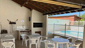 An outdoor patio with white plastic chairs and tables, a barbecue grill, and a view of a swimming pool.