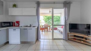 A modern kitchen with a dishwasher, microwave, and coffee maker. There is a dining area with a table and chairs, and a TV on a stand. - Kaz Mitan Appt. les Pieds Dans Leau ! (Les Trois-Îlets)