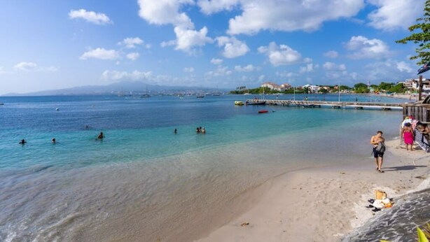A beach with clear turquoise water, a pier, and a few people swimming. - Kaz Mitan Appt. les Pieds Dans Leau ! (Les Trois-Îlets)