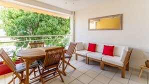 A balcony with a wooden table and chairs, a white sofa with red cushions, and a ceiling fan. - Kaz Mitan Appt. les Pieds Dans Leau ! (Les Trois-Îlets)