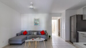 A modern living room with a grey sectional sofa, a small white coffee table, and a kitchen area with a refrigerator. - Kaz Mitan Appt. les Pieds Dans Leau ! (Les Trois-Îlets)