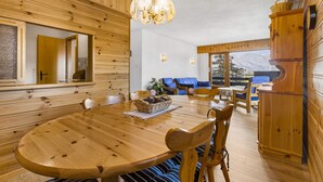 A wooden interior with a round dining table, chairs, a chandelier, and a view of the outdoors. - Christiania I F2 - 4 pers - près des pistes (Haute-Nendaz)