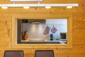A kitchen with wooden paneling, a stainless steel range hood, a microwave, and hanging kitchen utensils.