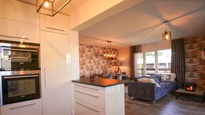 Une cuisine moderne dotée d’appareils électroménagers intégrés, un coin repas agrémenté d’un mur en pierre, et un espace salon confortable avec un canapé et une table basse.