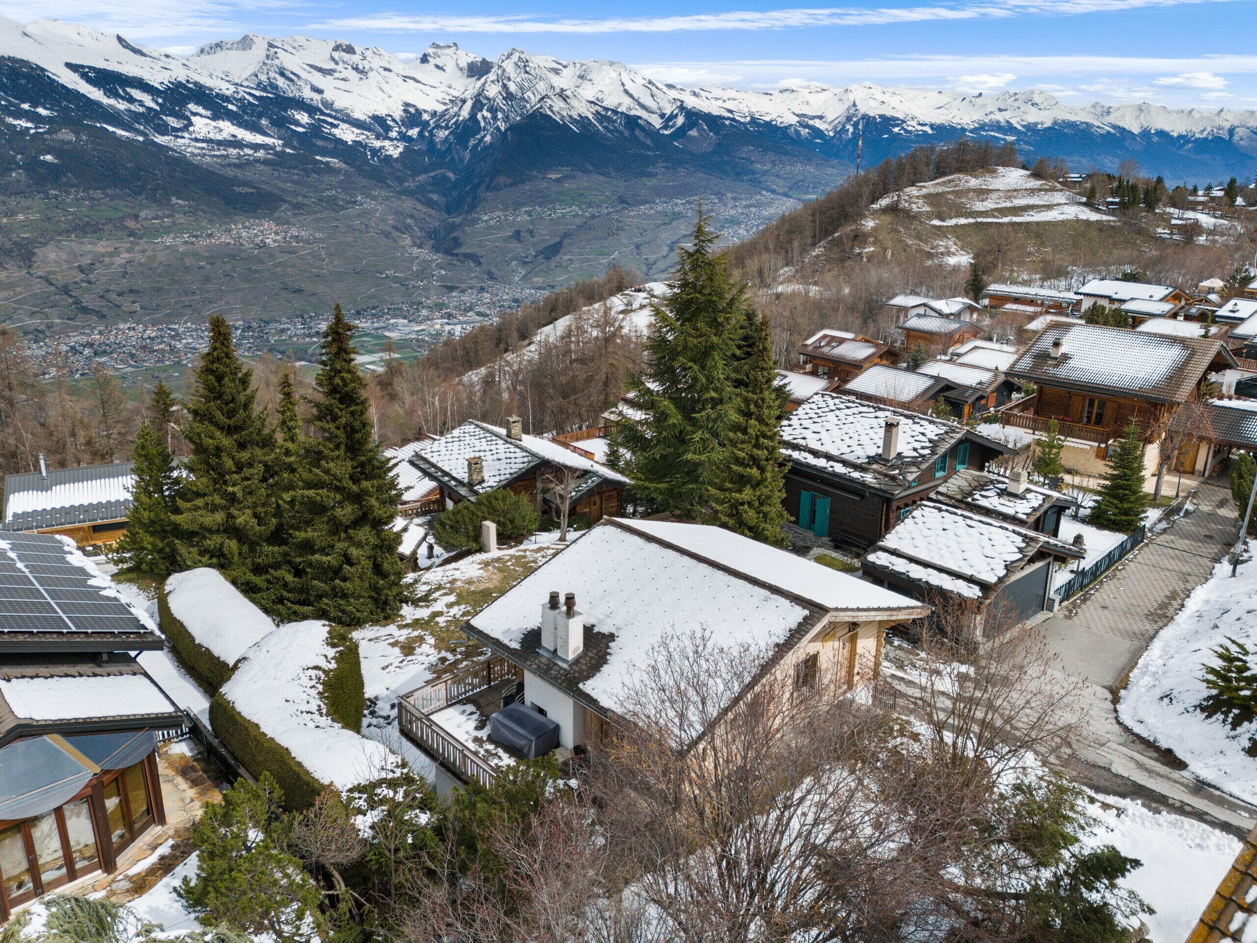 A snow-covered mountain village with traditional wooden houses and a view of snow-capped peaks in the background.