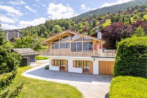 Een chalet met twee verdiepingen, een balkon, grote ramen en een oprit naar de ingang.