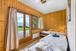 Een kamer met houten lambrisering, twee bedden, een groot raam en uitzicht op groen.