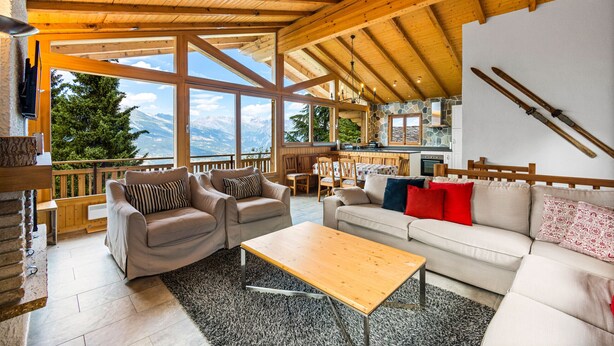 A spacious living area with wooden beams, large windows, and a view of mountains.