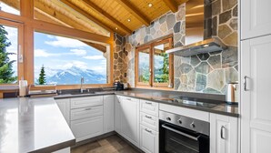 A modern kitchen with white cabinets, a stone accent wall, and a view of mountains.