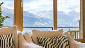 A room with a large window overlooking a mountainous landscape. There are two beige armchairs with striped pillows.
