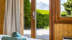 A wooden room with a bed, a window, and a view of mountains.