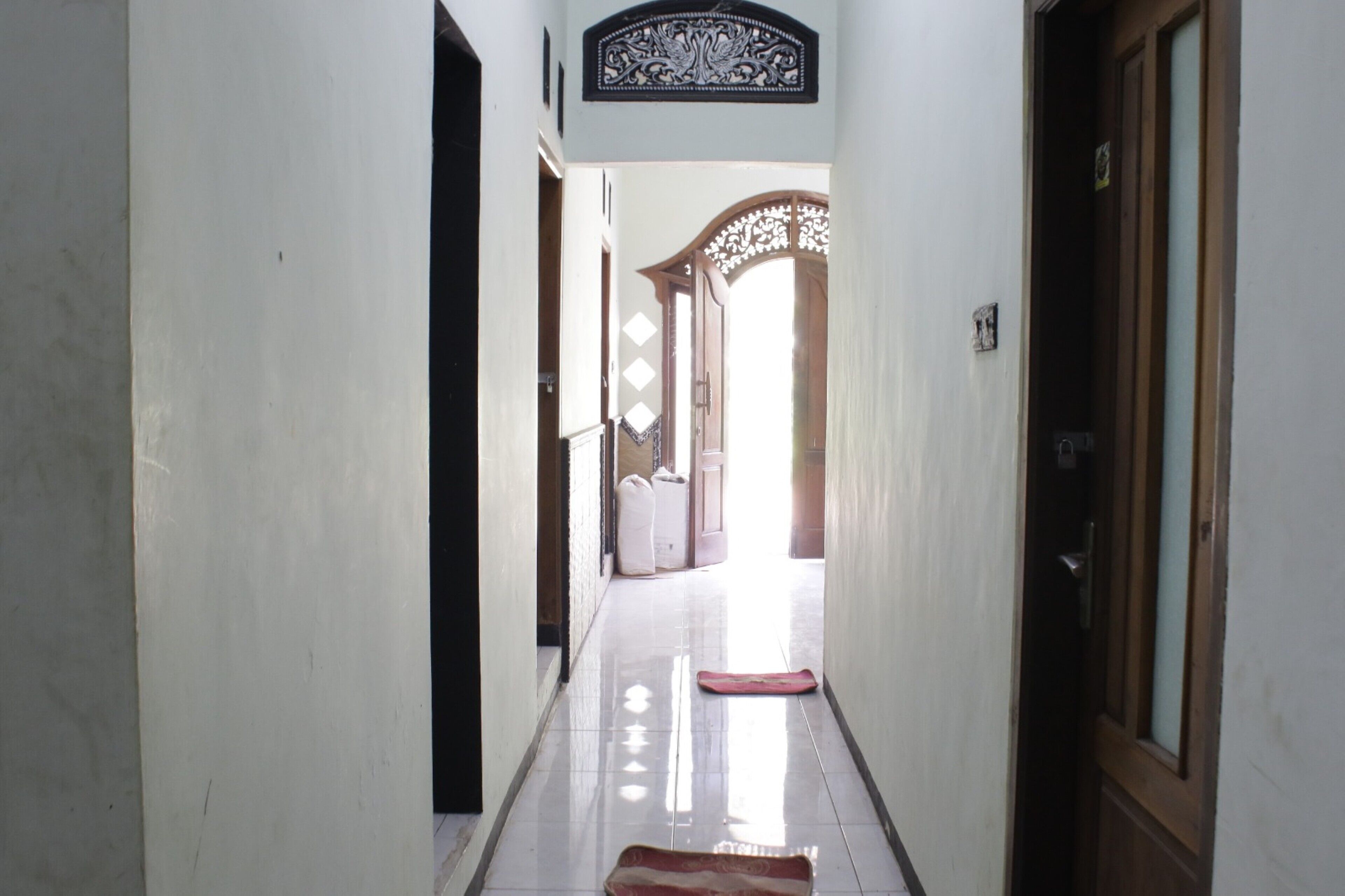 A narrow hallway with a polished floor, a decorative wooden door frame, and a light fixture above.
