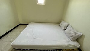 A small, single-bed room with a plain white mattress and pillow, a small window, and tiled flooring. - OYO Life  92982 Kost Berkah Ibu (Singasari)