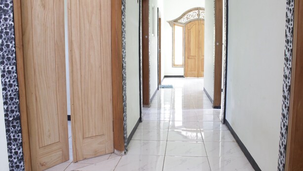A hallway with wooden doors and tiled flooring. - OYO Life  92982 Kost Berkah Ibu (Singasari)