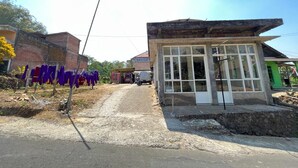 A small building with a single door and large windows, located at the end of a dirt road. - OYO Life  92982 Kost Berkah Ibu (Singasari)