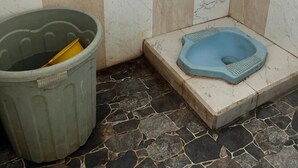 A small bathroom with a toilet, a trash bin, and tiled walls. - OYO Life  92982 Kost Berkah Ibu (Singasari)