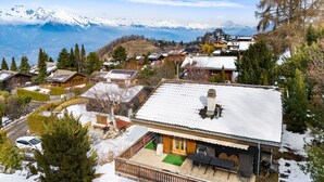 A snow-covered mountain village with traditional wooden houses, a wooden deck, and a view of snow-capped mountains in the background. - Darjean - 8 pers - belle vue (Haute-Nendaz)