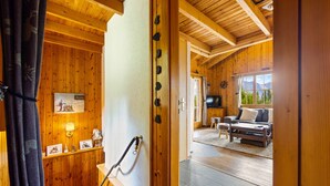 A wooden interior with a wooden door, a shelf with framed pictures, and a view of a living room with a sofa and a television. - Darjean - 8 pers - belle vue (Haute-Nendaz)
