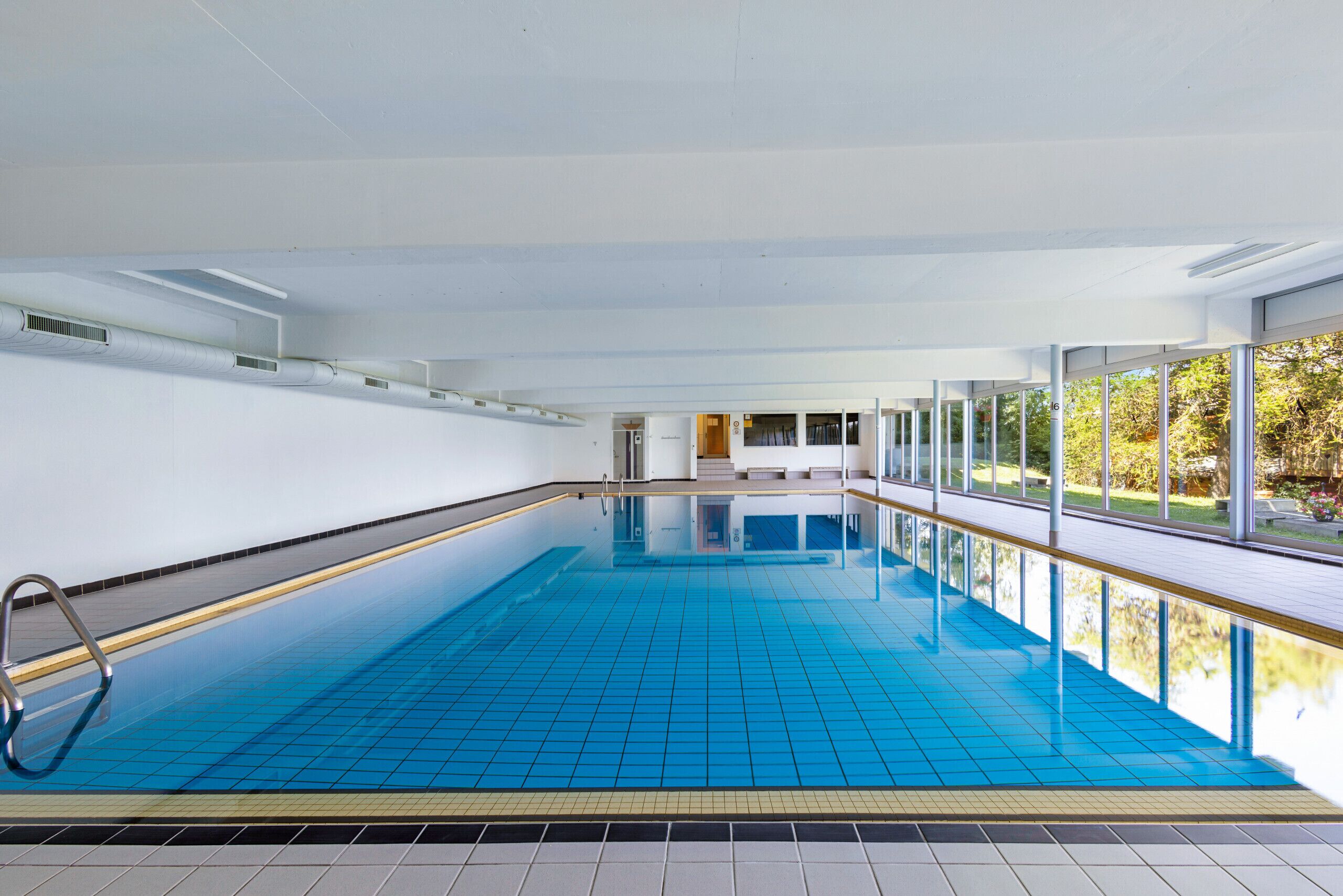 Ein großer, überdachter Schwimmbereich mit Glaswänden, gefliestem Boden und einer Metallleiter.
