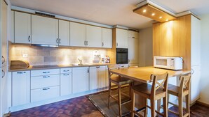 A compact kitchen with white cabinets, a wooden table, and a microwave. - Quille du Diable 35 - 4 pers - piscine (Haute-Nendaz)