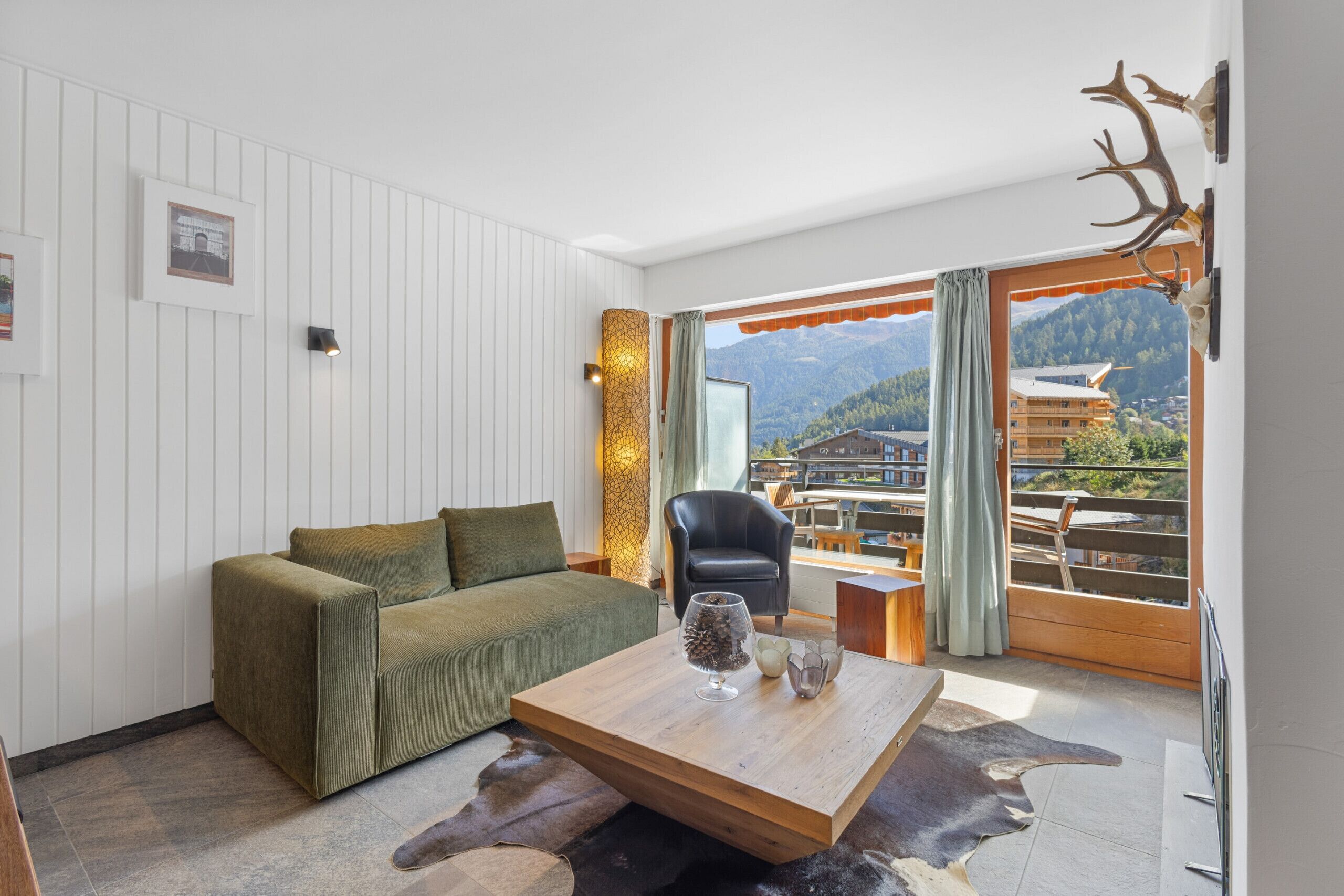 Ein modernes Wohnzimmer mit einer Couch, einem Couchtisch und Blick auf Berge durch große Fenster.