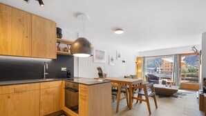 A modern kitchen with wooden cabinets, a central island, and a dining area with a table and chairs. - Les Platanes E4 - 5 pers - centre station (Haute-Nendaz)
